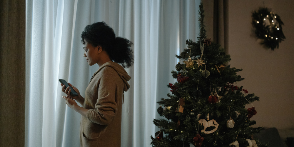 woman standing by Christmas tree looking at phone 